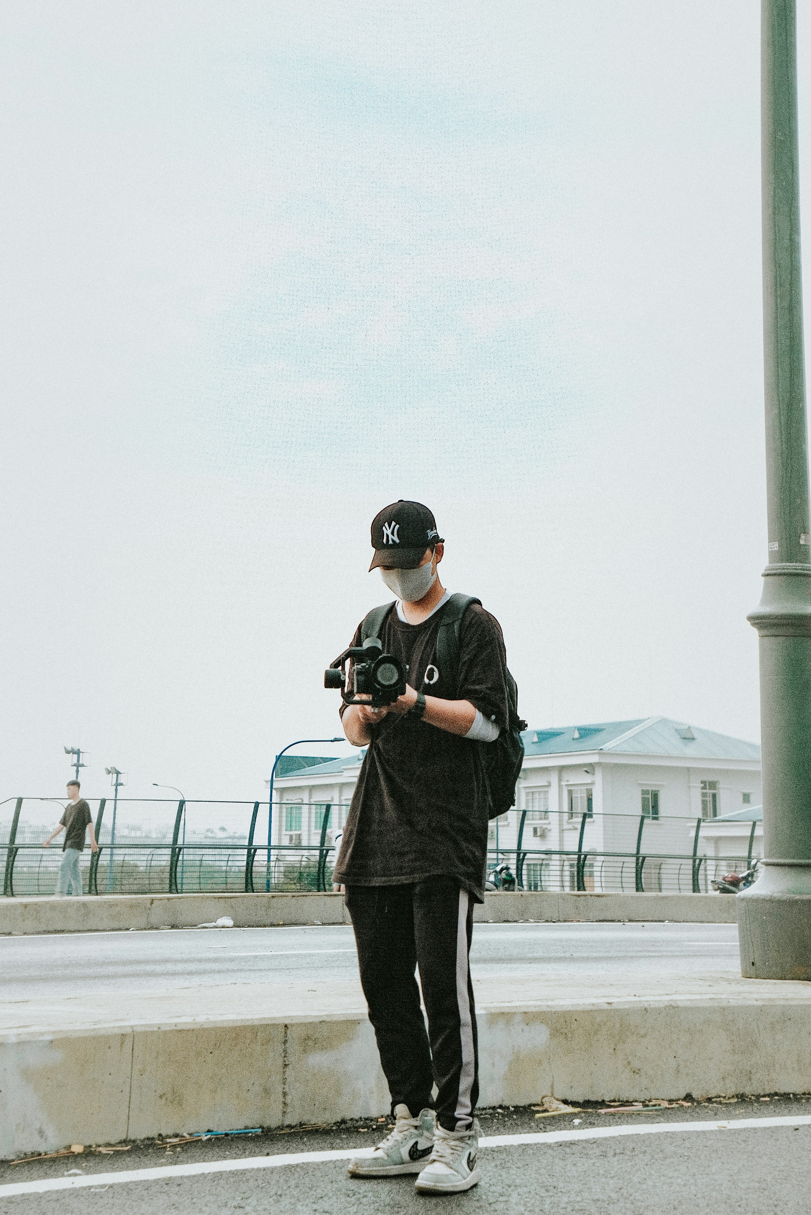 man in black jacket and black pants holding black dslr camera standing on gray concrete floor